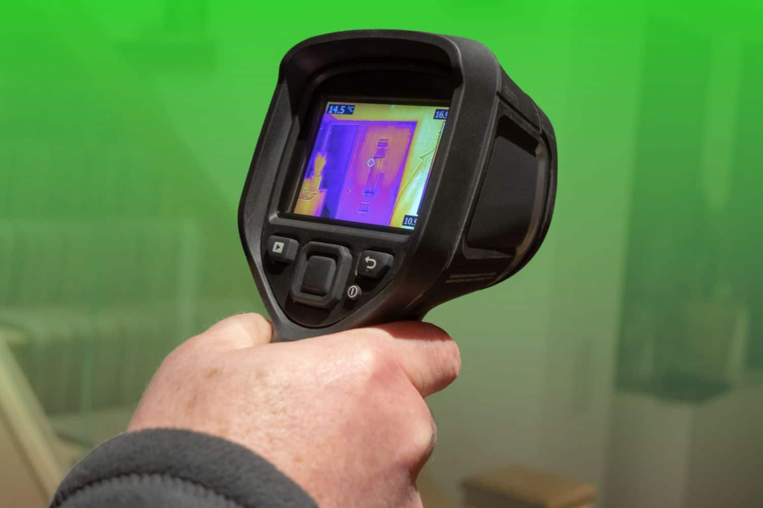 A hand holding a handheld thermal imaging camera displaying an infrared heat map scan of an interior doorway.