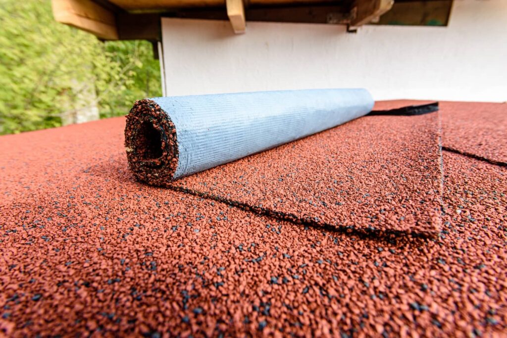 Part of a Roof With Red Roll Roofing Being Installed