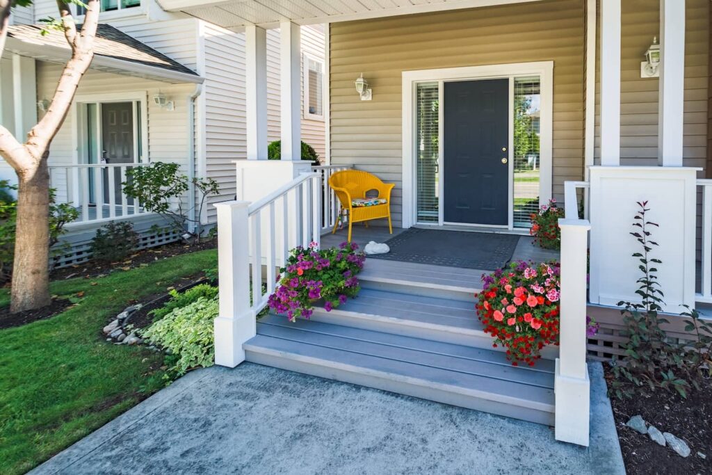 Front porch steps with a doormat and greenery/plants in planters.