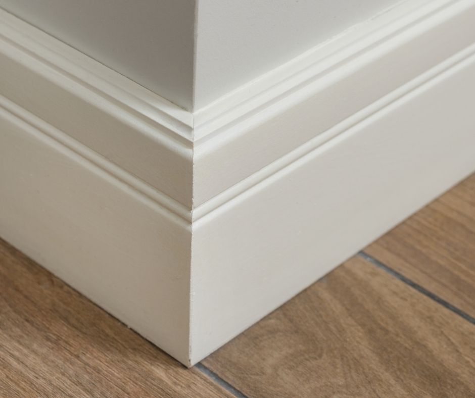 Close-up of white painted baseboard molding joining neatly at an outside wall corner above a wood plank floor.