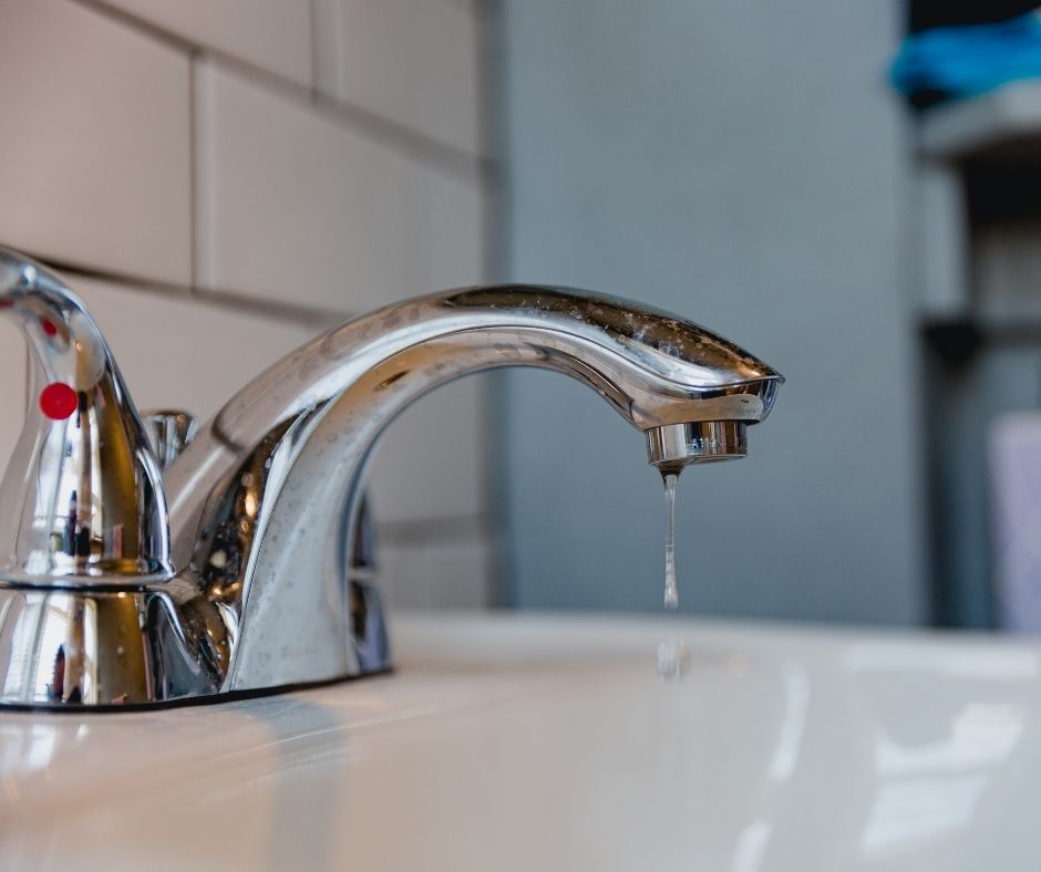 Close-up of a chrome bathroom sink faucet with water dripping from the spout into a white basin.